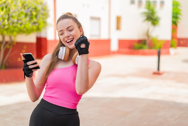 Young pretty sport girl at outdoors with phone in victory position