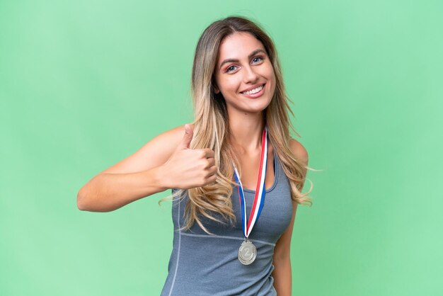 Young pretty sport Uruguayan woman with medals over isolated background giving a thumbs up gesture