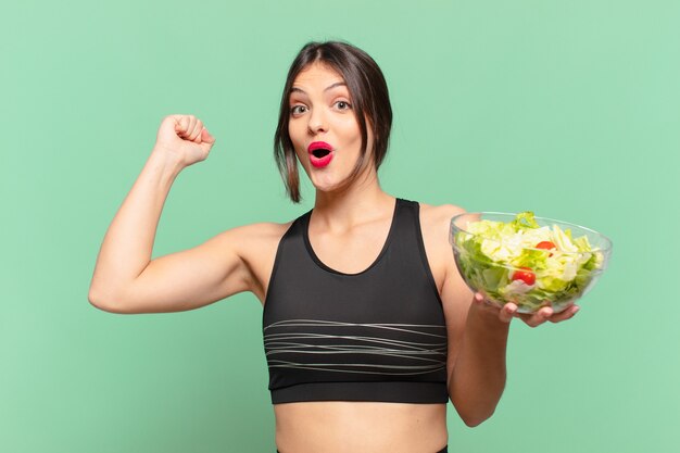 Young pretty sport woman celebrating successful a victory and holding a salad