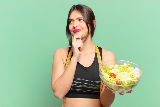 Young pretty sport woman doubting or uncertain expression and holding a salad