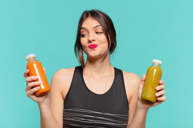 Young pretty sport woman doubting or uncertain expression and holding smoothy