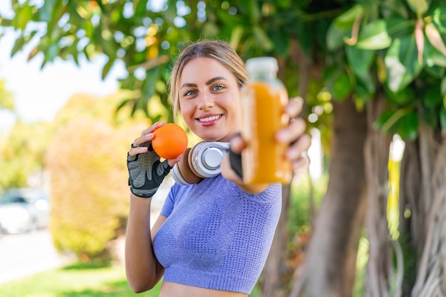 Foto giovane bella donna sportiva all'aperto che tiene un'arancia e un succo d'arancia