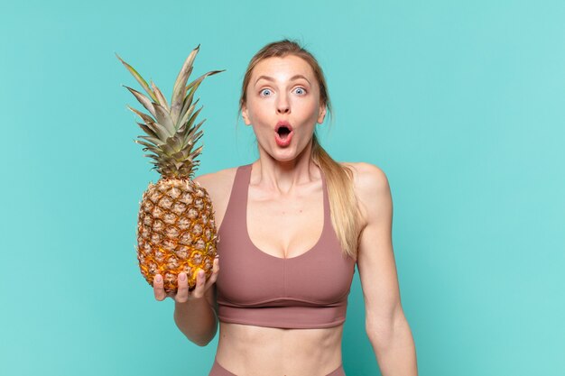 Young pretty sport woman scared expression and holding a pineapple