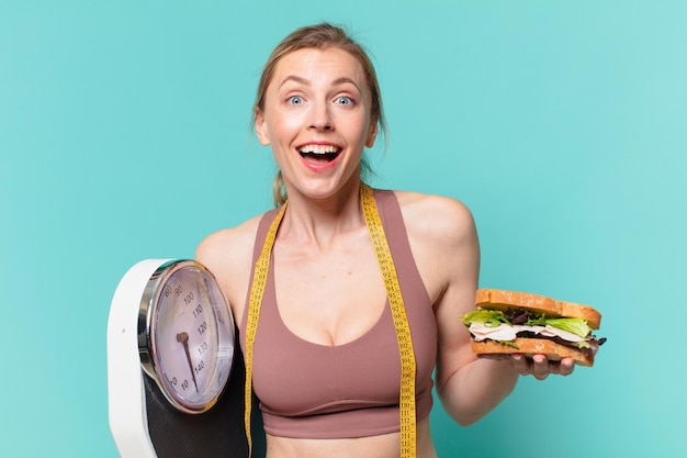 Giovane bella donna sportiva espressione sorpresa e con in mano una bilancia e un panino