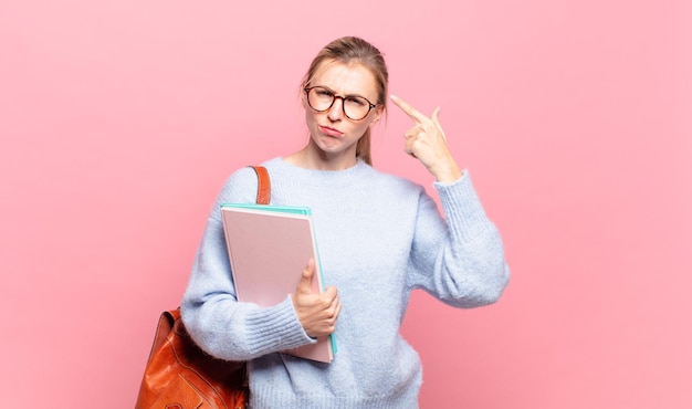 Young pretty student feeling confused and puzzled, showing you are insane, crazy or out of your mind