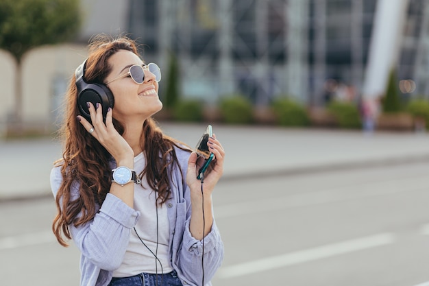 Young pretty student girl waiting for a taxi car, and listening to music