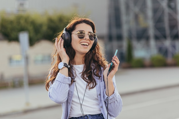 Young pretty student girl waiting for a taxi car, and listening to music