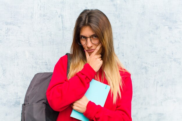 Giovane studentessa carina che sembra seria, riflessiva e diffidente, con un braccio incrociato e la mano sul mento, opzioni di ponderazione