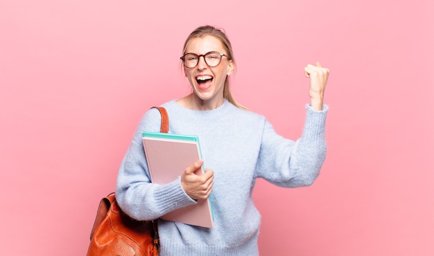 Young pretty student shouting aggressively with an angry expression or with fists clenched celebrating success