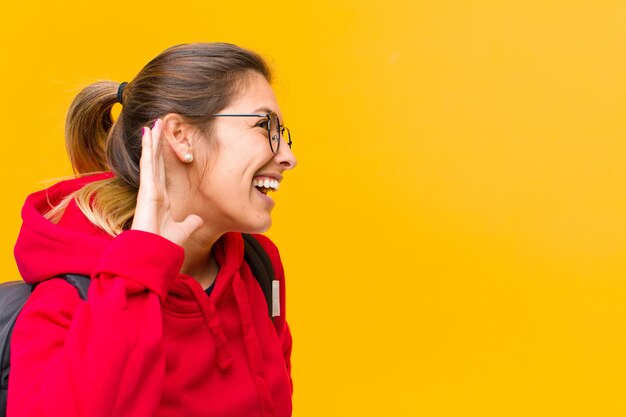 Young pretty student smiling, looking curiously to the side, trying to listen to gossip or overhearing a secret