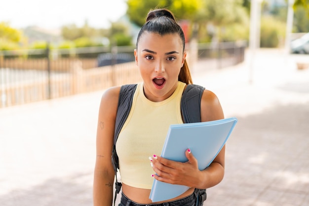 屋外で驚きとショックを受けた表情を持つ若いかわいい学生女性