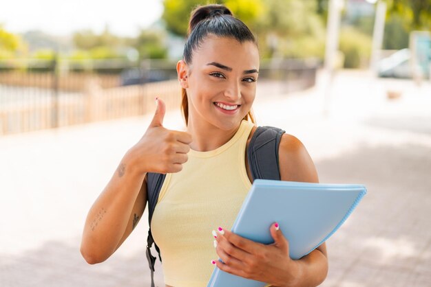 Young pretty student woman at outdoors with thumbs up because something good has happened