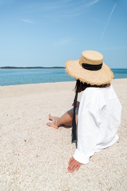 Молодая красивая стильная женщина сидит на пляже и смотрит на море. копировать пространство