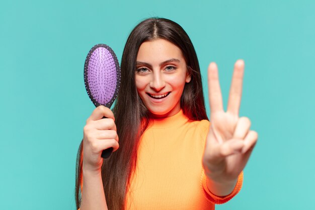 Young pretty teenager girl doing victory sign and holding brush