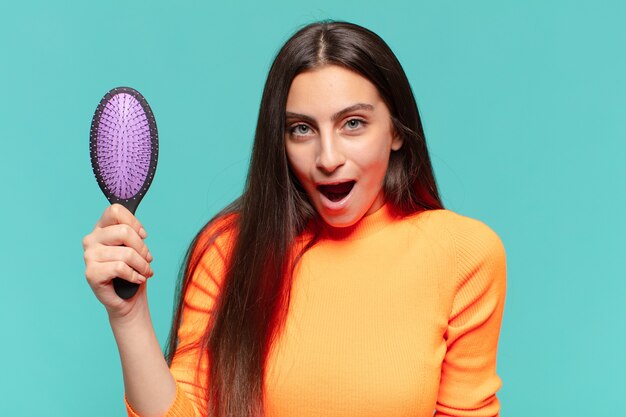 Young pretty teenager girl. shocked or surprised expression. hair brush concept