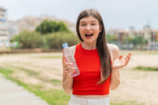 ショックを受けた表情で屋外で水のボトルを持つ若いかなりウクライナの女性