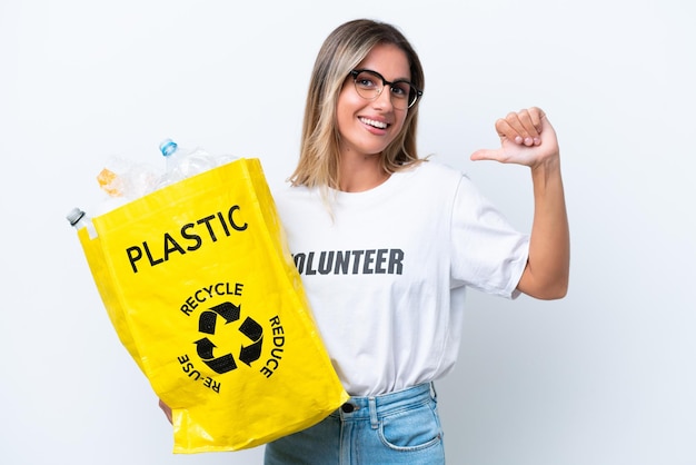 Young pretty Uruguayan woman holding a bag full of plastic bottles to recycle isolated on white background proud and selfsatisfied