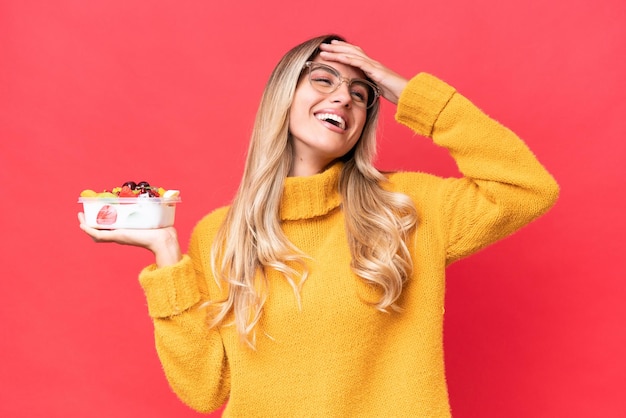 Young pretty Uruguayan woman holding a bowl of fruit isolated on red background smiling a lot