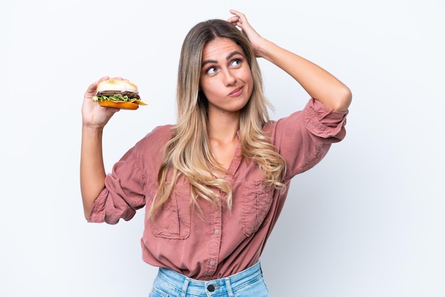 Foto giovane bella donna uruguaiana che tiene un hamburger isolato su sfondo bianco con dubbi e con espressione del viso confusa