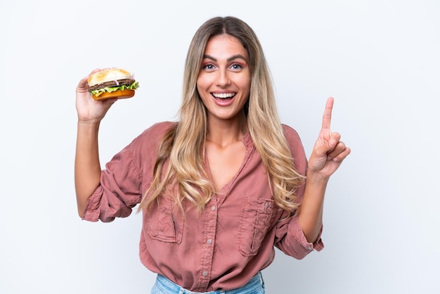 Молодая симпатичная уругвайская женщина держит бургер на белом фоне, указывая на отличную идею