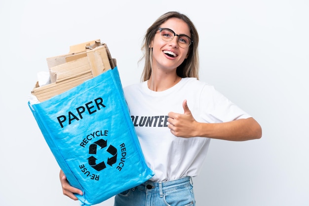 Young pretty Uruguayan woman holding a recycling bag full of paper to recycle isolated on white chroma background with thumbs up because something good has happened