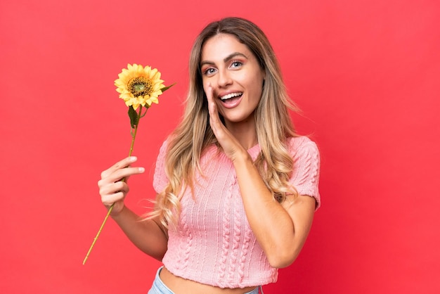 Photo young pretty uruguayan woman holding sunflower isolated on background whispering something