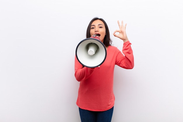 Young pretty woman against flat wall with a megaphone