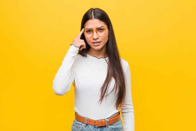 Young pretty woman against a yellow background showing a disappointment gesture with forefinger.