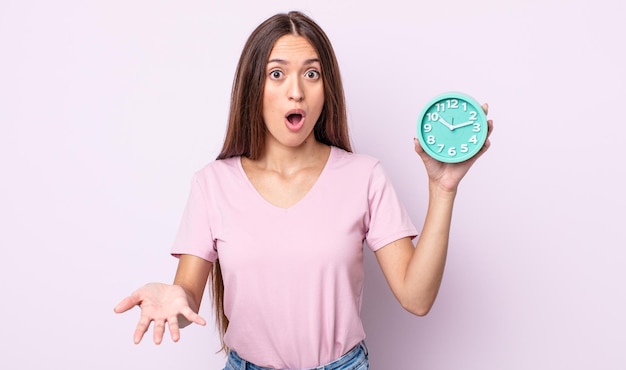 Young pretty woman amazed, shocked and astonished with an unbelievable surprise. alarm clock concept