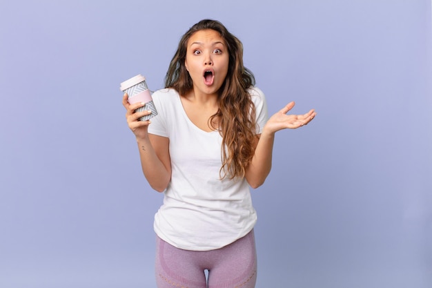 Young pretty woman amazed, shocked and astonished with an unbelievable surprise and holding a coffee