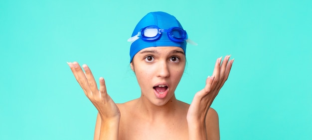 Young pretty woman amazed, shocked and astonished with an unbelievable surprise with swimming goggles