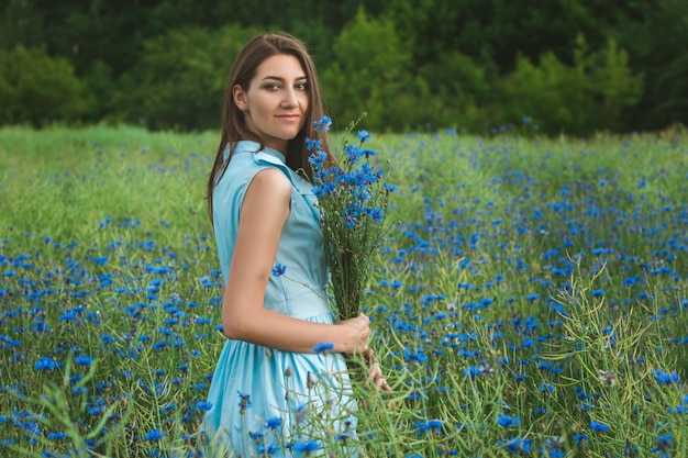 Giovane donna graziosa tra il campo di bei fiordalisi