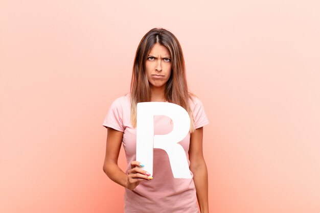 Young pretty woman angry, anger, disagreement, holding the letter R of the alphabet to form a word or a sentence