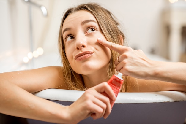 Foto giovane e bella donna che applica la crema per il viso in bagno