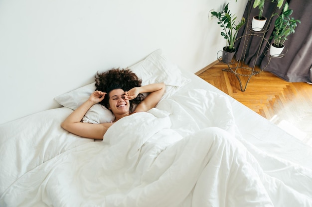 Foto giovane donna graziosa a letto con lenzuola bianche luce intensa