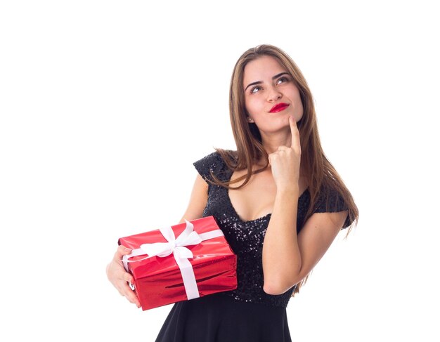 Young pretty woman in black dress holding red present and looking up on white background in studio