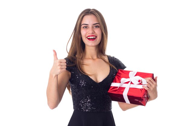 Young pretty woman in black dress holding red present and looking up on white background in studio