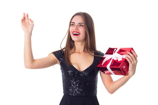 Young pretty woman in black dress holding red present and looking up on white background in studio