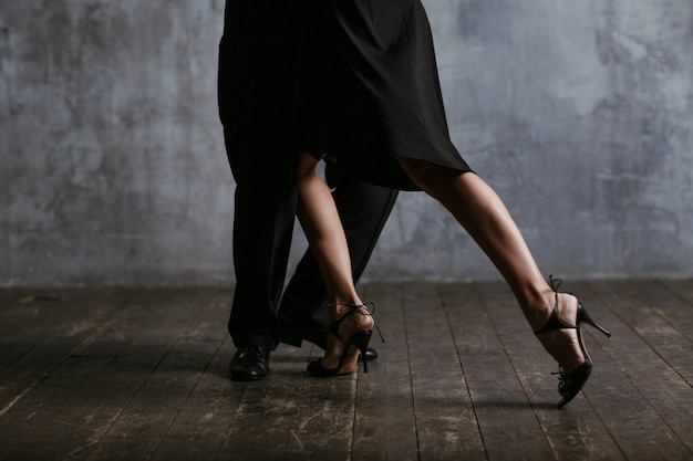 Young pretty woman in black dress and man dance tango. Legs close up.