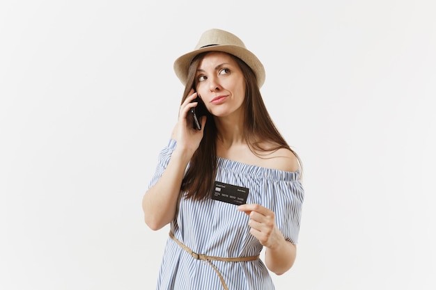 Young pretty woman in blue dress, hat talking on mobile phone, conducting pleasant conversation, holding credit card isolated on white background. People, banking concept. Advertising area. Copy space