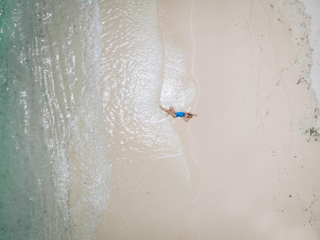 Young pretty woman in a blue swimming suit lying on a sandy beach during tide. Summer vacation concept