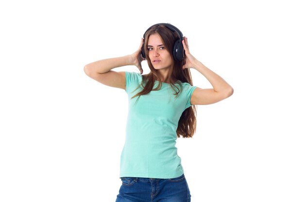 Young pretty woman in blue T-shirt and jeans  in black headphones on white background in studio