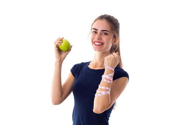 Young pretty woman in blue Tshirt with centimeter around her neck biting green apple in studio