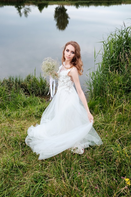 Giovane donna graziosa (sposa) in abito da sposa bianco all'aperto, trucco e acconciatura