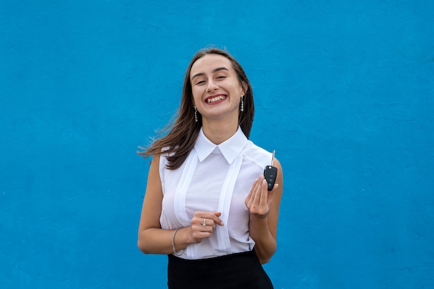 Young pretty woman in business cloth hold car key on blue background