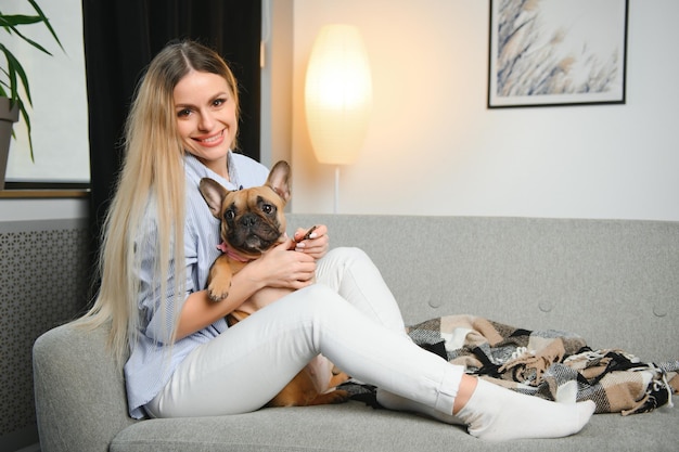 Young pretty woman in casual clothes hugging her dog sitting on the sofa in the living room of her cozy country house Animal communication concept