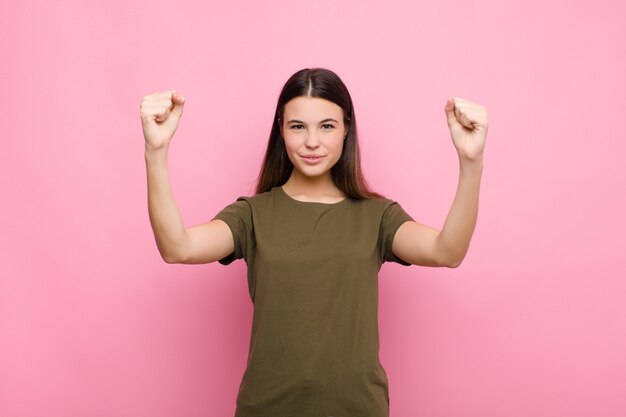 Young pretty woman celebrating an unbelievable success like a winner, looking excited and happy saying take that! over pink wall