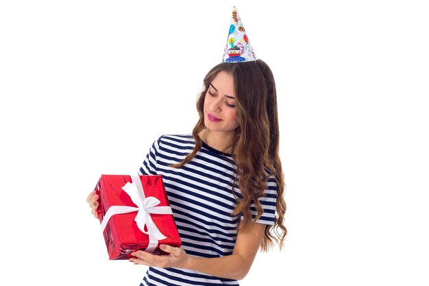 Young pretty woman in celebration cap with long hair holding red present and looking at it