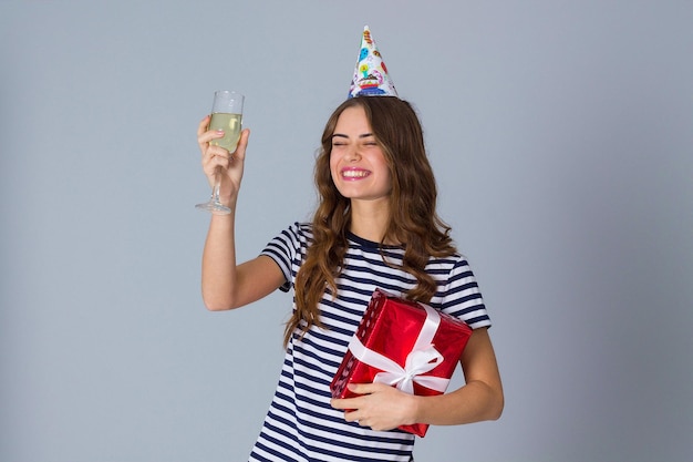 Young pretty woman in celebration cap with long hair holding red present and looking at it