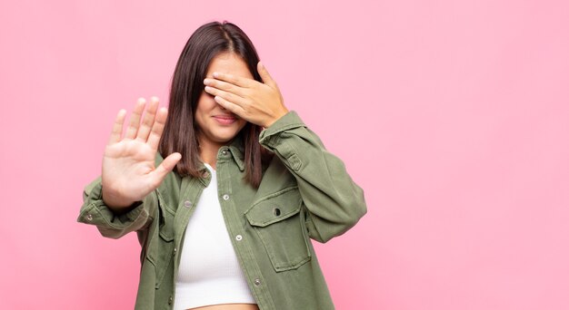 Young pretty woman covering face with hand and putting other hand up